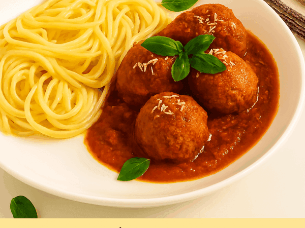 Almôndegas ao sugo caseiras servidas em um prato fundo branco ao lado de espaguete, cobertas com molho de tomate, queijo parmesão ralado e folhas frescas de manjericão.