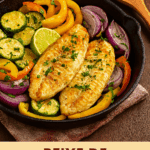 Dois filés de peixe grelhado em uma frigideira de ferro fundido, cercados por legumes salteados como abobrinha, pimentão amarelo e cebola roxa, e finalizados com salsinha e uma fatia de limão.