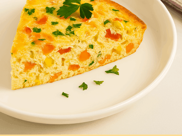 Omelete de Forno Fofinha (Saudável e Sem Fritura) Uma fatia alta de omelete de forno fofinho servida em um prato branco, mostrando um recheio colorido de milho, cenoura e pimentão, e decorada com uma folha de salsinha fresca.