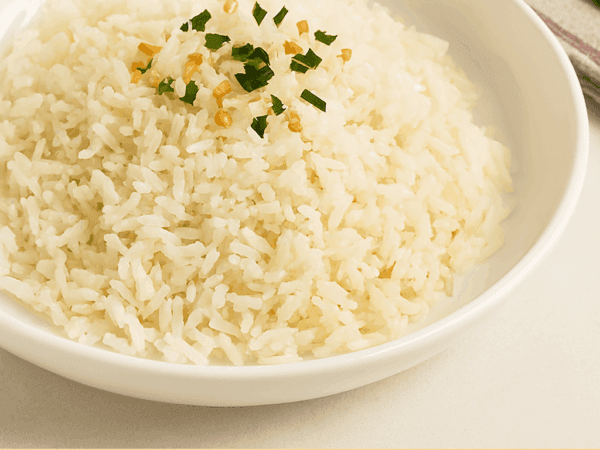 Uma porção de arroz branco soltinho servido em um prato fundo branco, finalizado com pedacinhos de alho frito dourado e cheiro-verde picado.