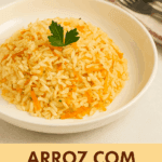Arroz com cenoura ralada soltinho, servido em formato de montinho em um prato fundo branco e finalizado com uma folha de salsinha fresca por cima.