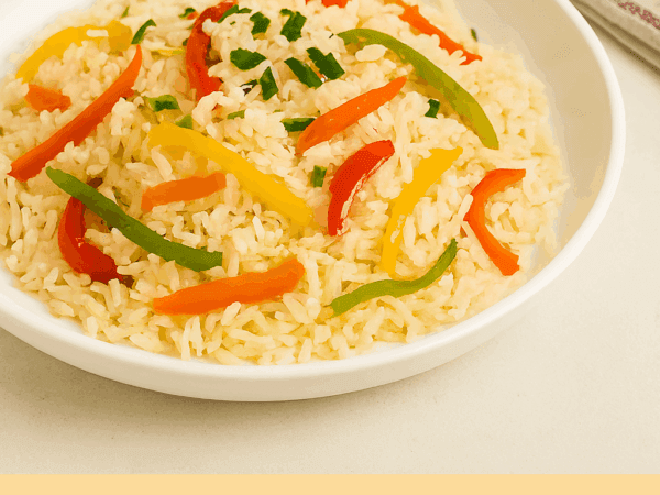 Arroz com pimentão servido em um prato fundo branco, misturado com tiras coloridas de pimentão vermelho, verde e amarelo, e salpicado com cheiro-verde picado.