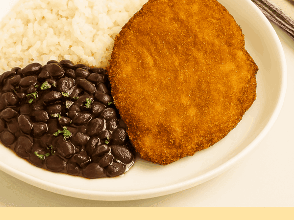 Bife à milanesa sequinho e dourado servido em um prato branco, acompanhado por uma porção de arroz branco e feijão preto salpicado com salsinha.