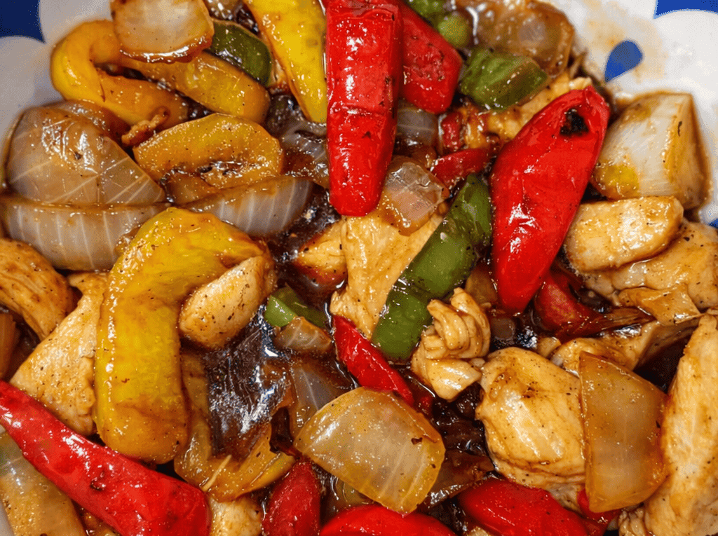 Frigideira com cubos de frango selados, pimentões coloridos e amendoim torrado, todos envolvidos por um molho agridoce espesso e brilhante.