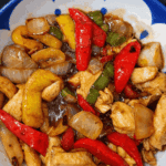 Frigideira com cubos de frango selados, pimentões coloridos e amendoim torrado, todos envolvidos por um molho agridoce espesso e brilhante.