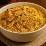 Farofa de manteiga dourada e soltinha servida em uma tigela branca, coberta com anéis de cebola crocante, pedacinhos de bacon e cheiro-verde picado.