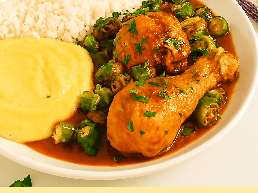 Frango com quiabo ensopado servido em um prato fundo branco, mostrando pedaços de frango (coxa e sobrecoxa) e quiabo em um molho rico, acompanhado de arroz branco e angu de milho cremoso.