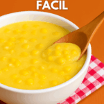 Creme de milho fácil e bem cremoso servido em uma tigela branca, com grãos de milho inteiros visíveis e uma colher de madeira, sobre um guardanapo xadrez vermelho.