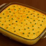 Travessa de vidro com escondidinho de bacalhau recém-saído do forno, com uma generosa cobertura de queijo derretido e gratinado bem dourado.