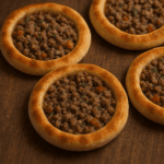 Esfihas abertas de carne recém-assadas com bordas douradas e fofinhas, recheio suculento de carne moída com tomate, servidas com limão.