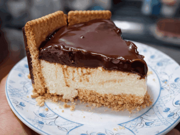 Travessa de vidro exibindo as camadas da Torta Holandesa: base crocante de biscoito, creme branco aveludado, cobertura brilhante de ganache de chocolate e laterais decoradas com biscoitos redondos Calipso.